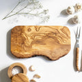Wooden cutting board with garlic, salt, and cutlery on a white background.