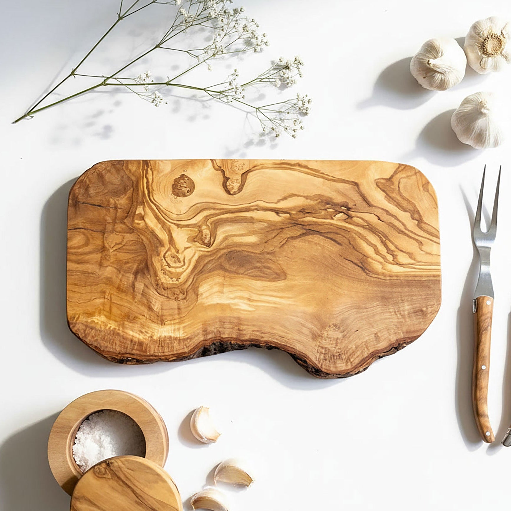 Wooden cutting board with garlic, salt, and cutlery on a white background.