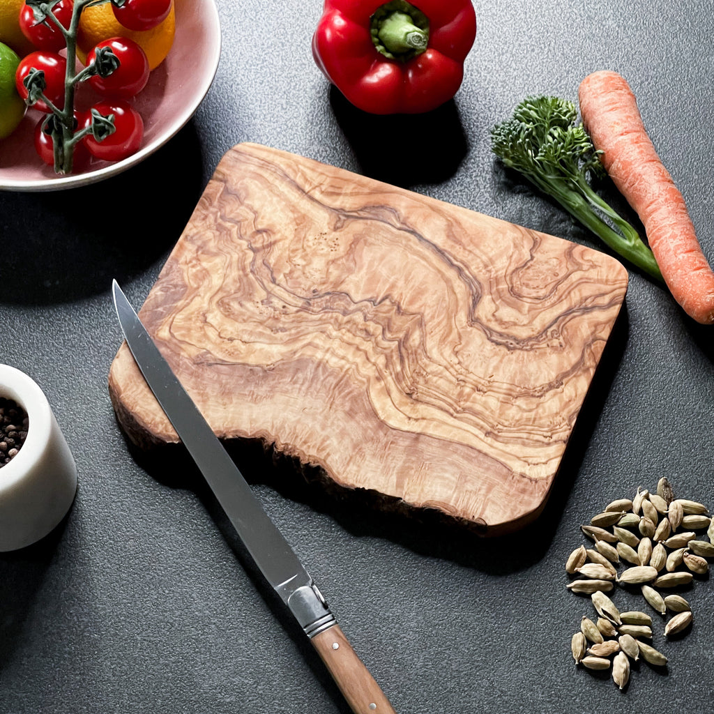 a rustic olive wood board with some food and cooking accessories