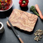 a rustic olive wood board with some food and cooking accessories