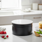 Black and white cake tin on a kitchen counter with berries and a cake.