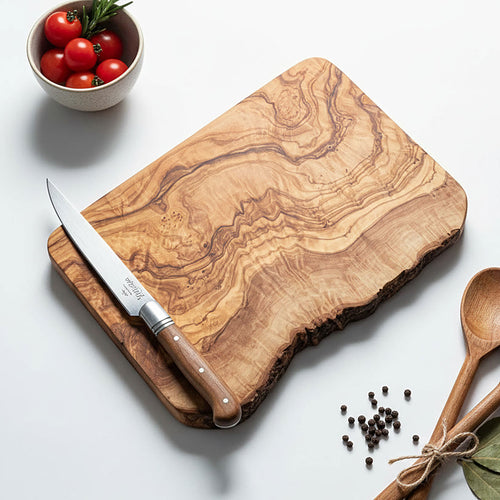 Wooden cutting board with knife and bowl of tomatoes on a white surface