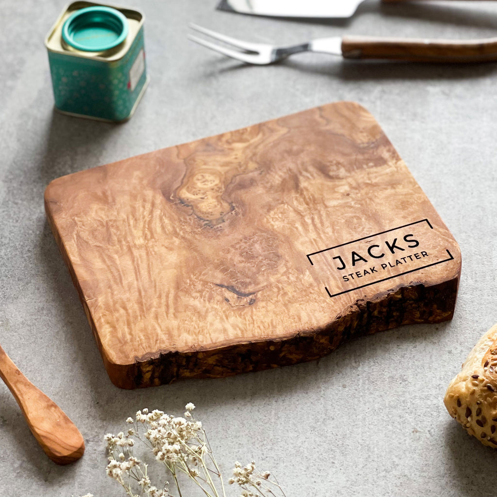 Wooden cutting board with 'JACKS' engraving on a grey surface with a some accessories scattered around.