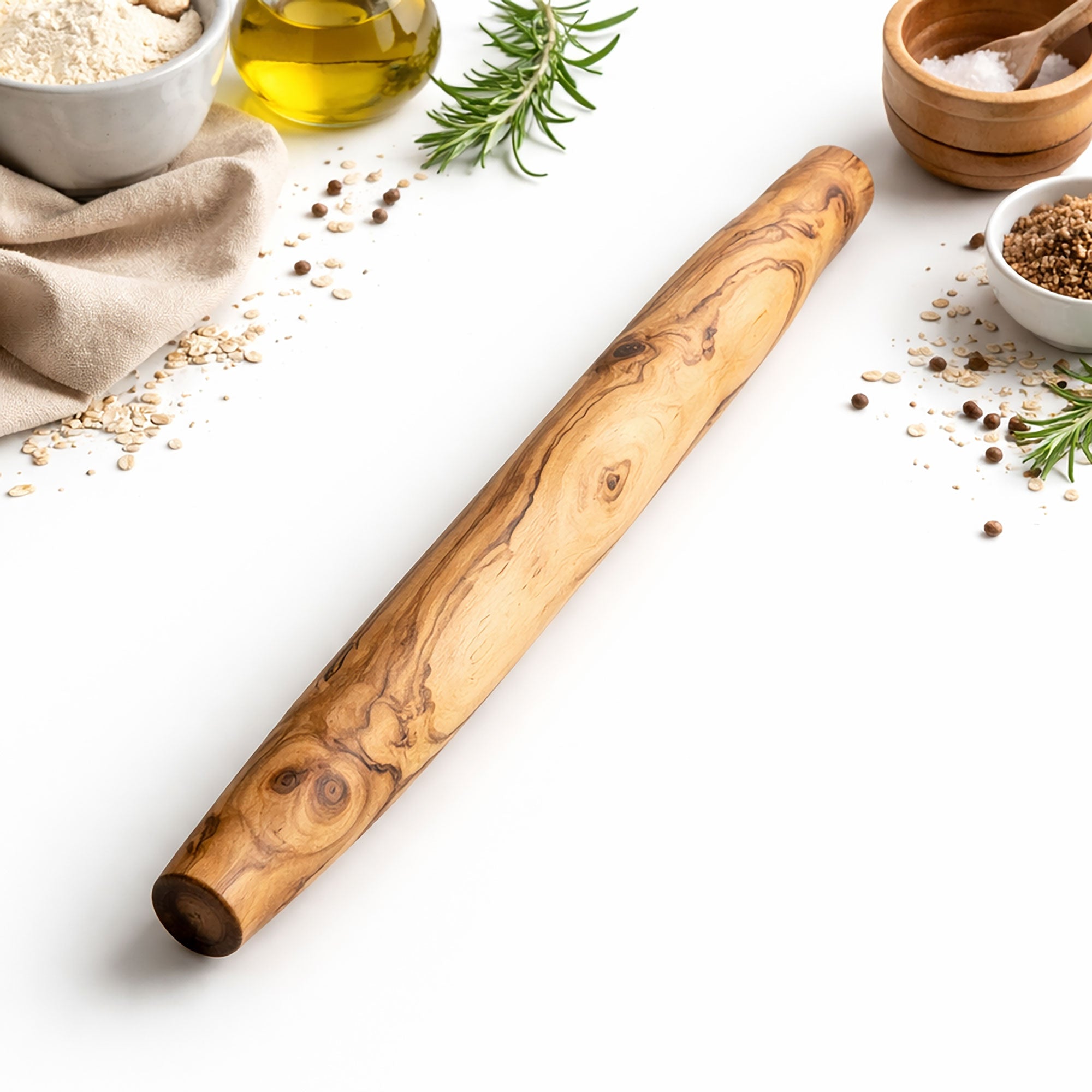 Wooden french-style rolling pin on a white surface with kitchen ingredients in the background
