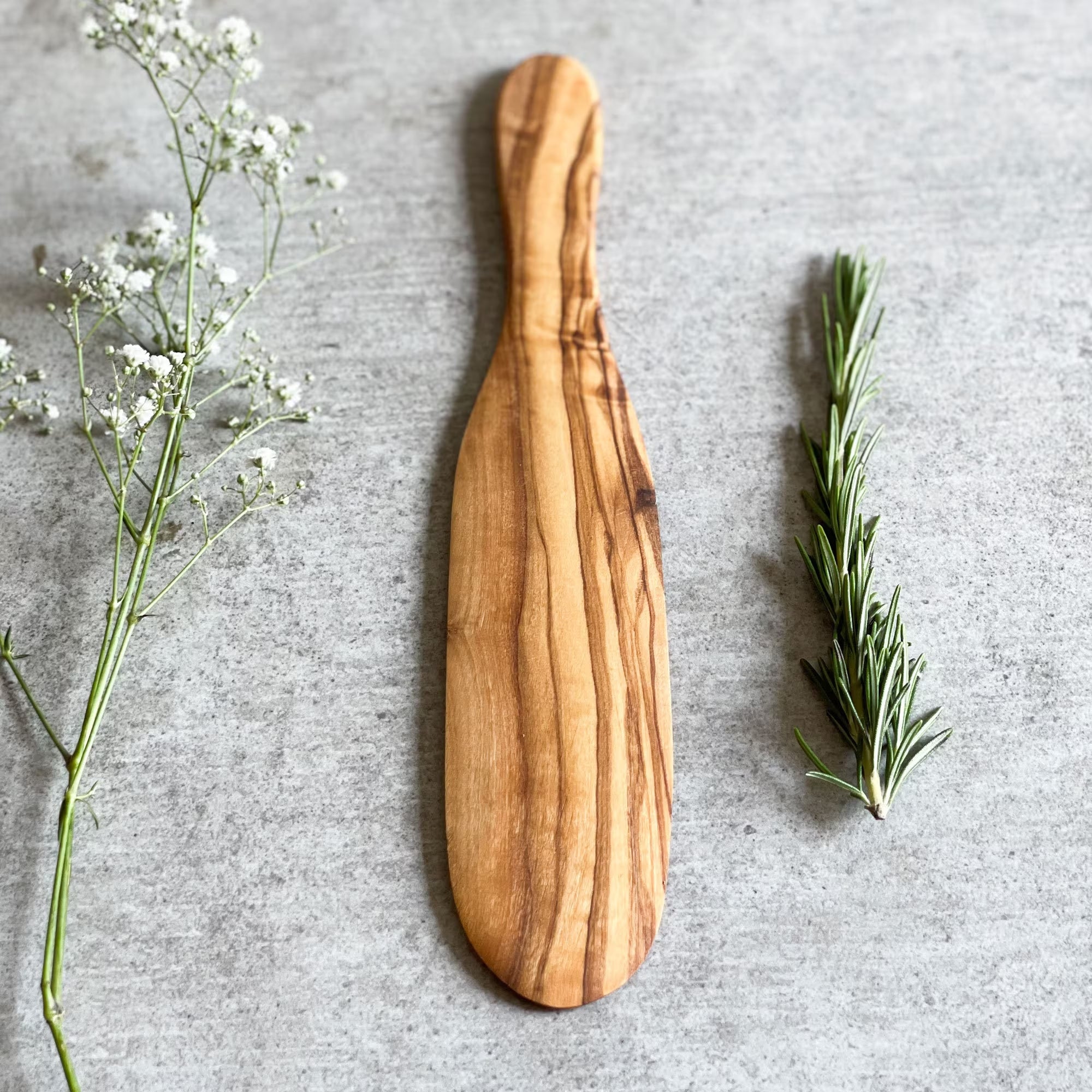 wooden spatula on a grey surface with a flower and some herbs