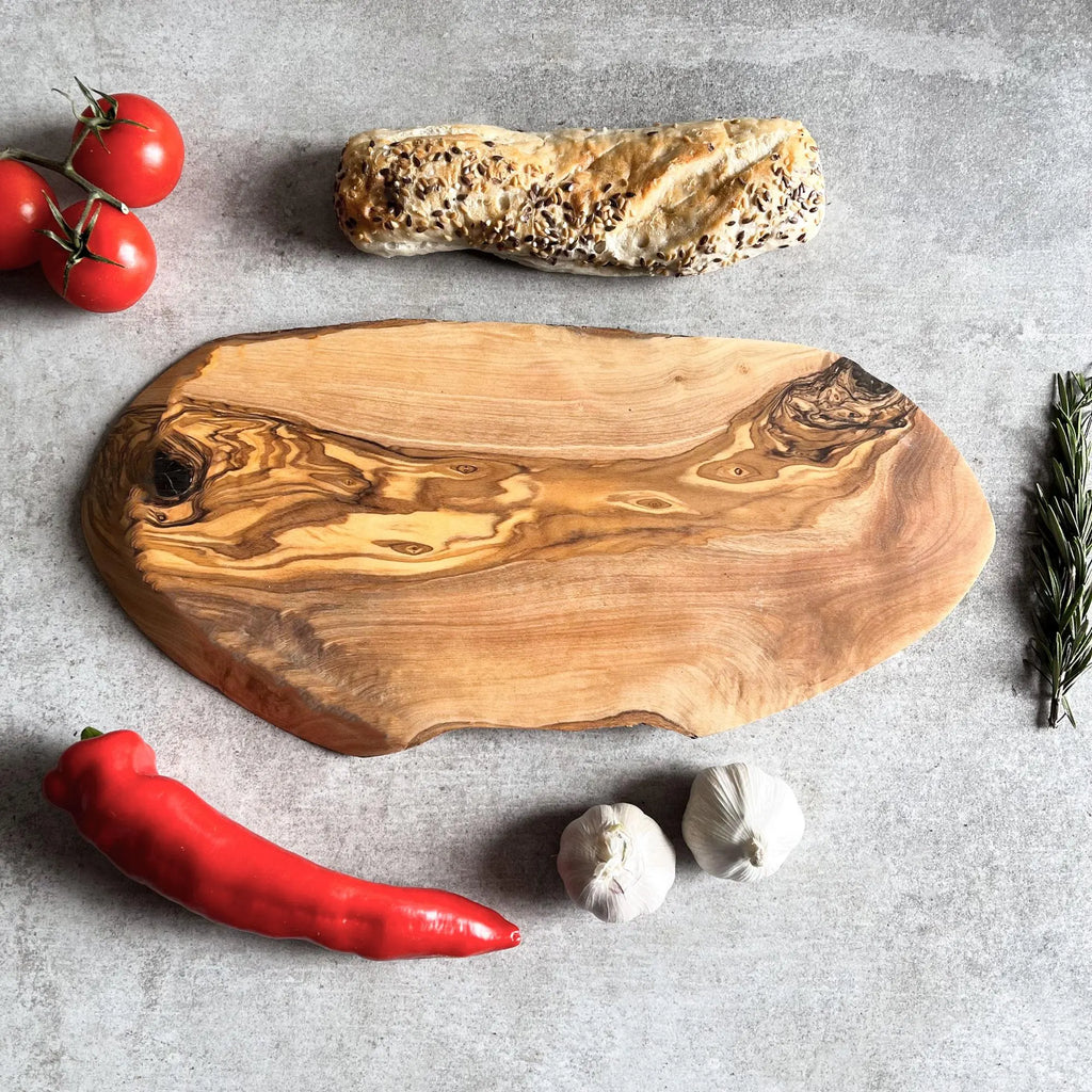 A rustic oval olive wood cheese board displayed with bread, tomatoes, garlic, and herbs.
