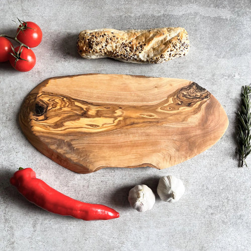 A rustic oval olive wood cheese board displayed with bread, tomatoes, garlic, and herbs.