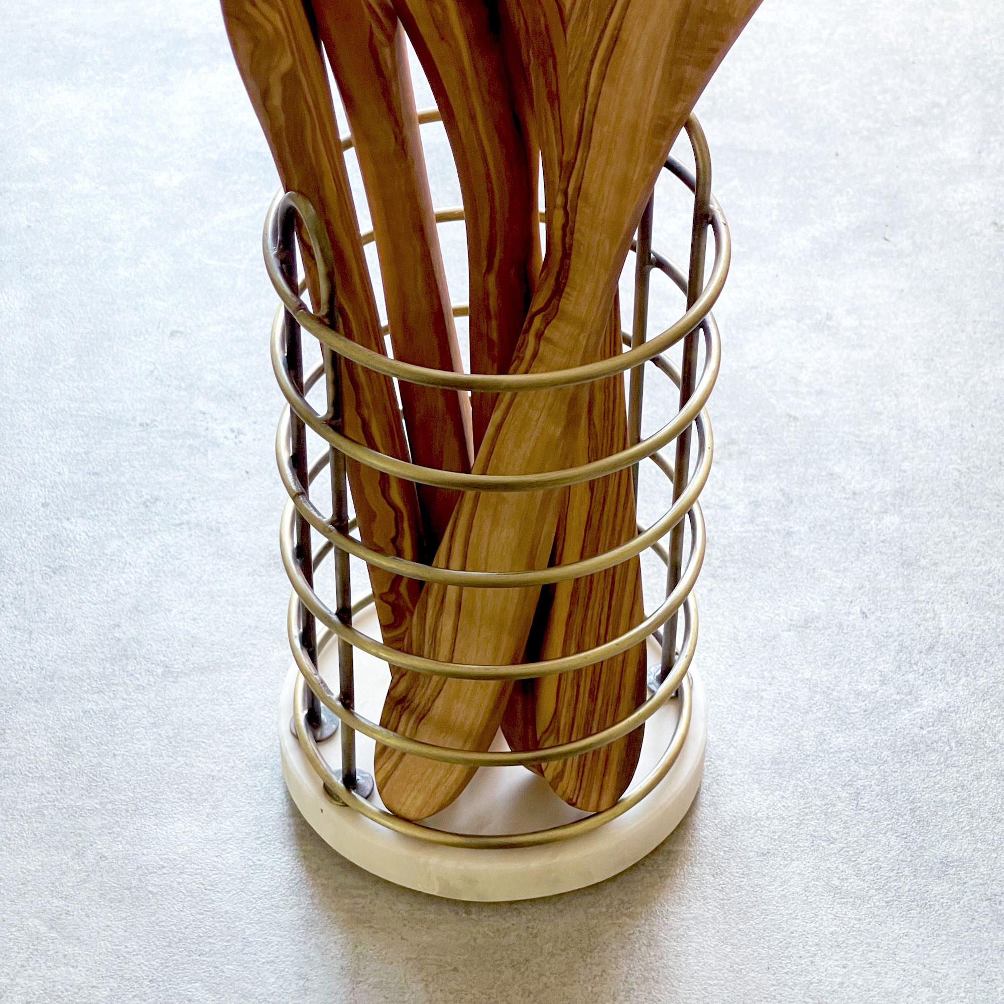 Wooden utensils in a gold metal holder on a light gray background