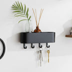Black wall-mounted shelf with hooks holding keys and decorative items against a white wall.