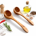 Wooden ladles on a white surface with kitchen items like oil, salt, and herbs.