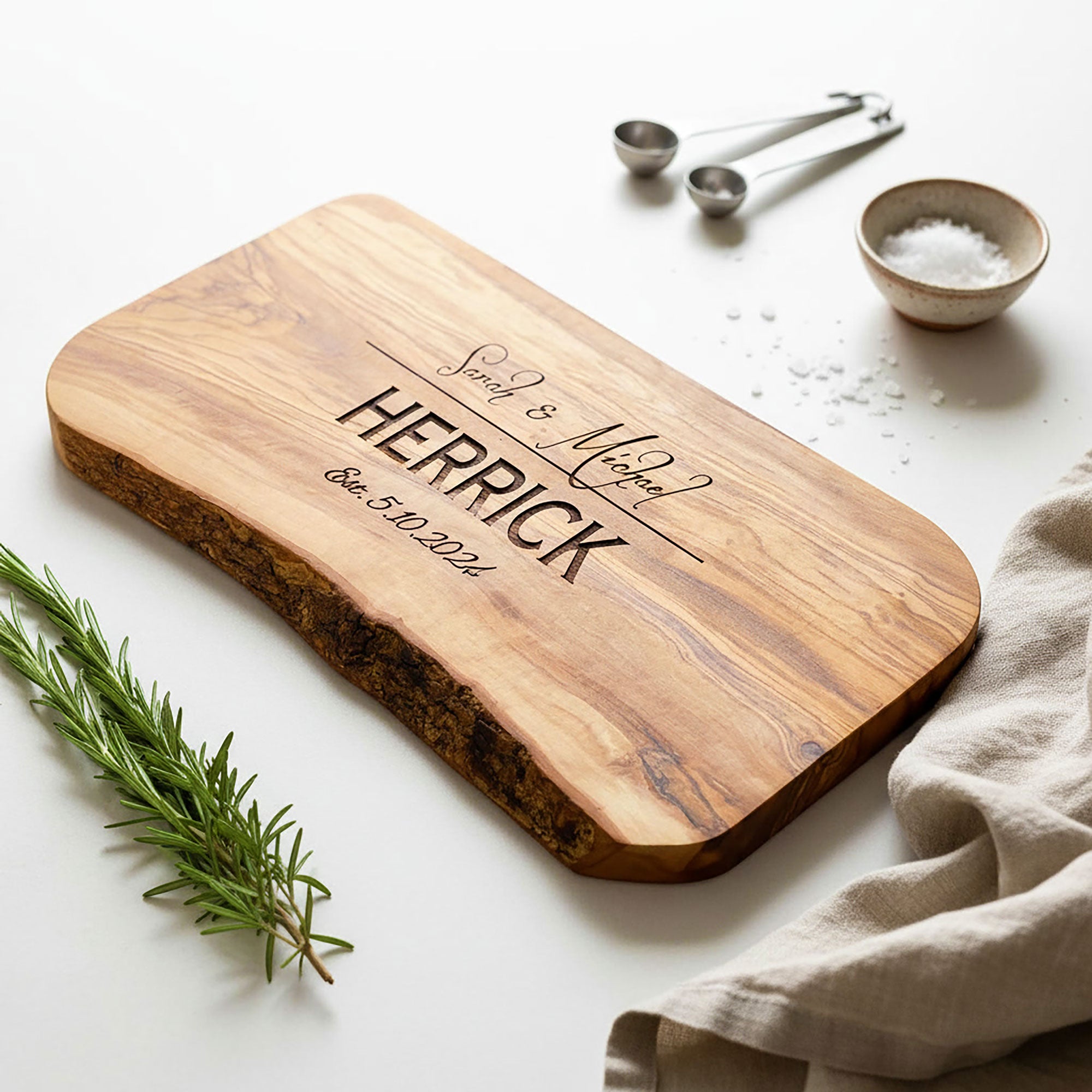 Wooden cutting board with engraved text on a white surface with kitchen items.