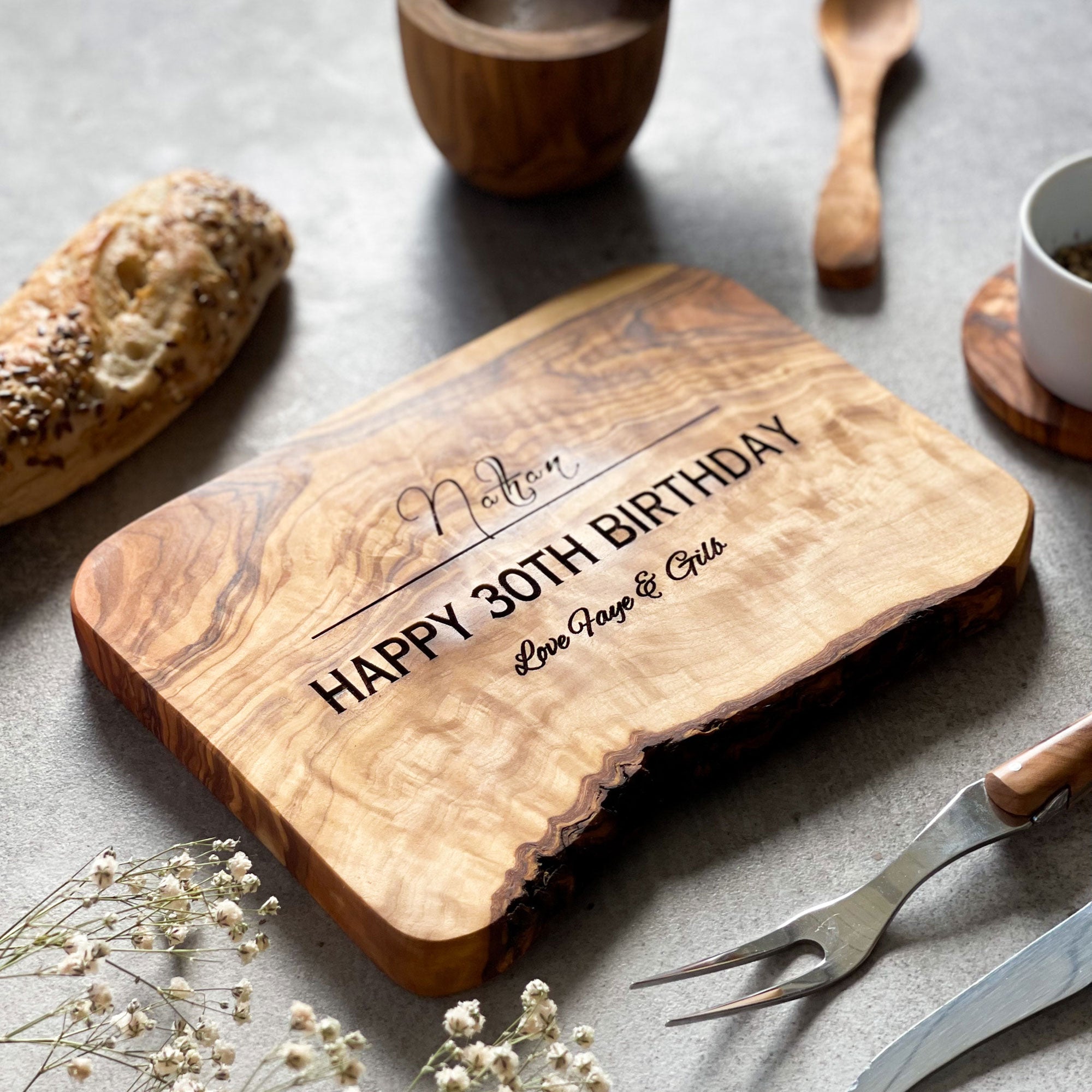 Wooden cutting board with engraved text on a grey surface with kitchen items.