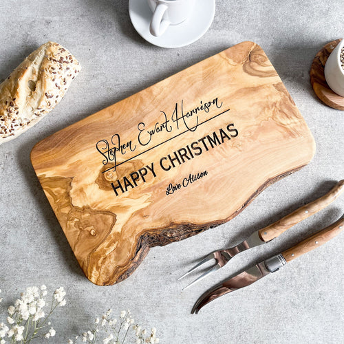 Wooden cutting board with engraved text on a grey surface with serving fork and knife.