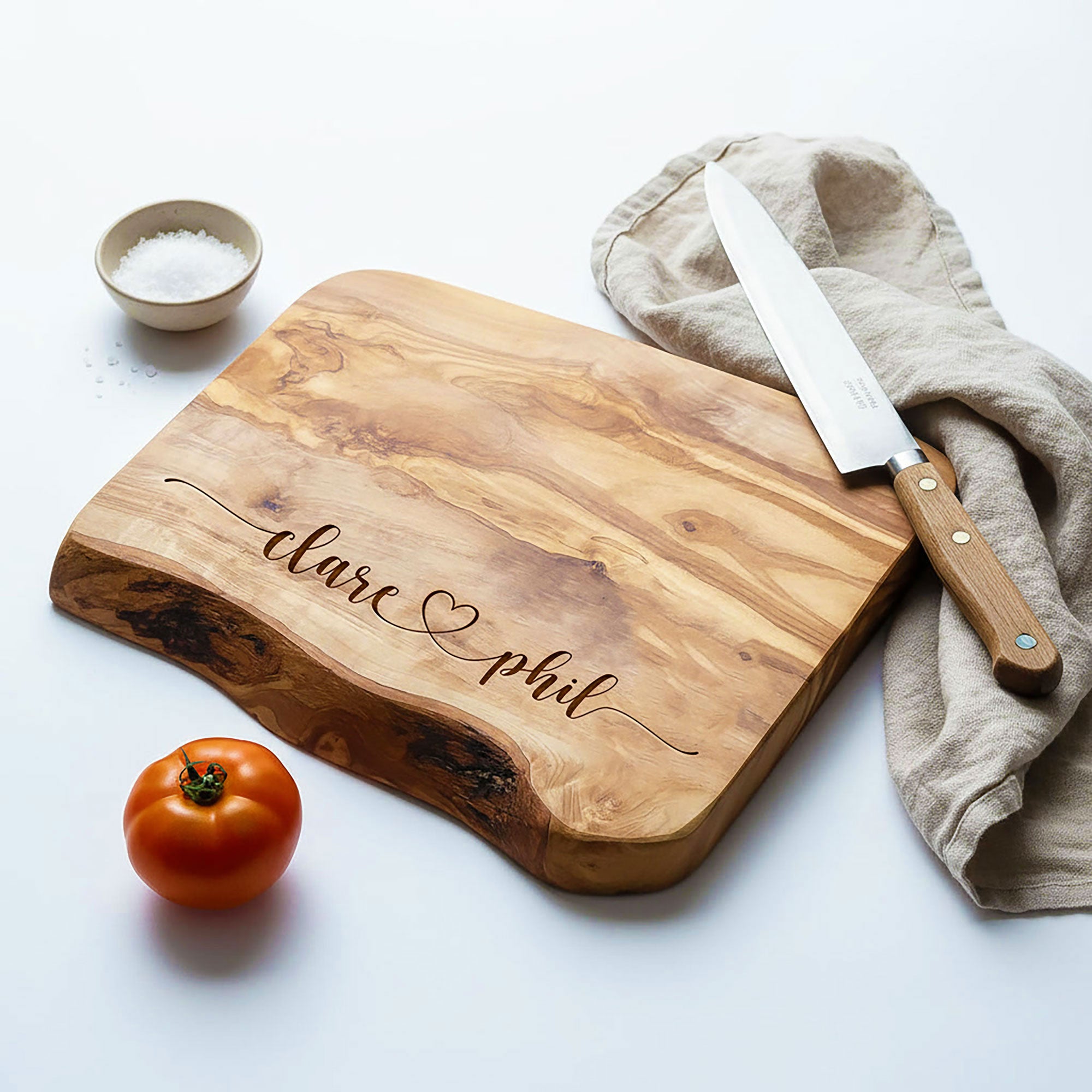 Wooden cutting board with engraved names, knife, and tomato on a white background