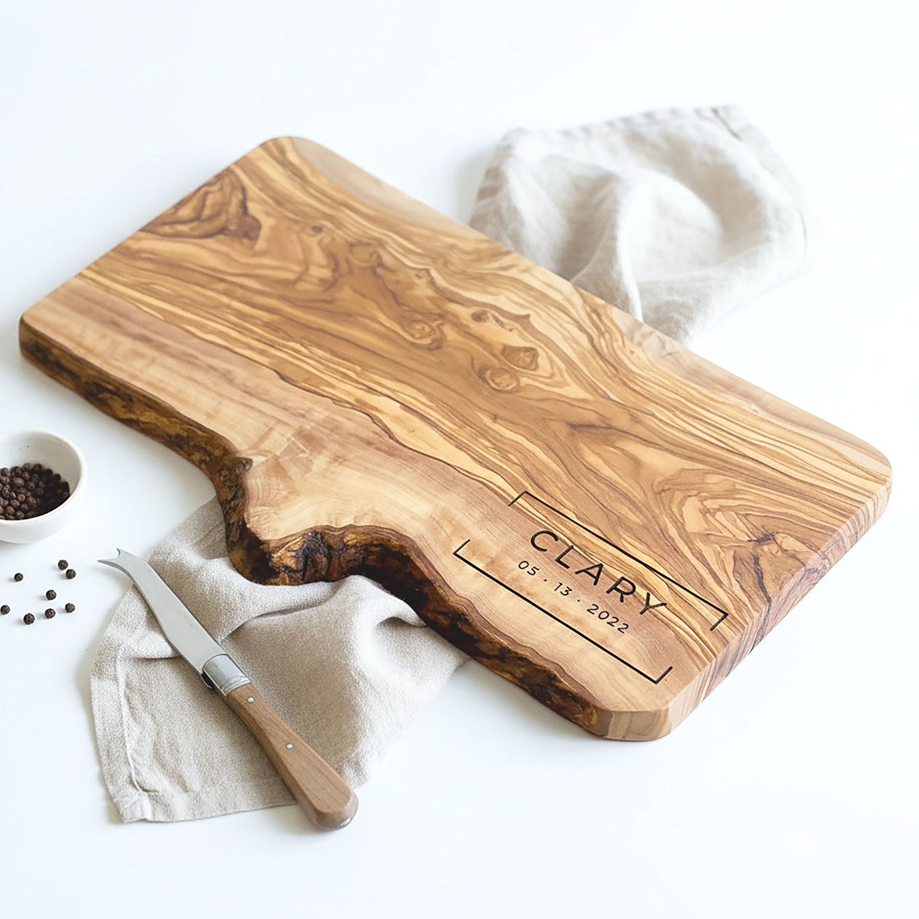 Wooden cutting board with 'CLARY' engraving on a white surface with a knife and bowl of spices.