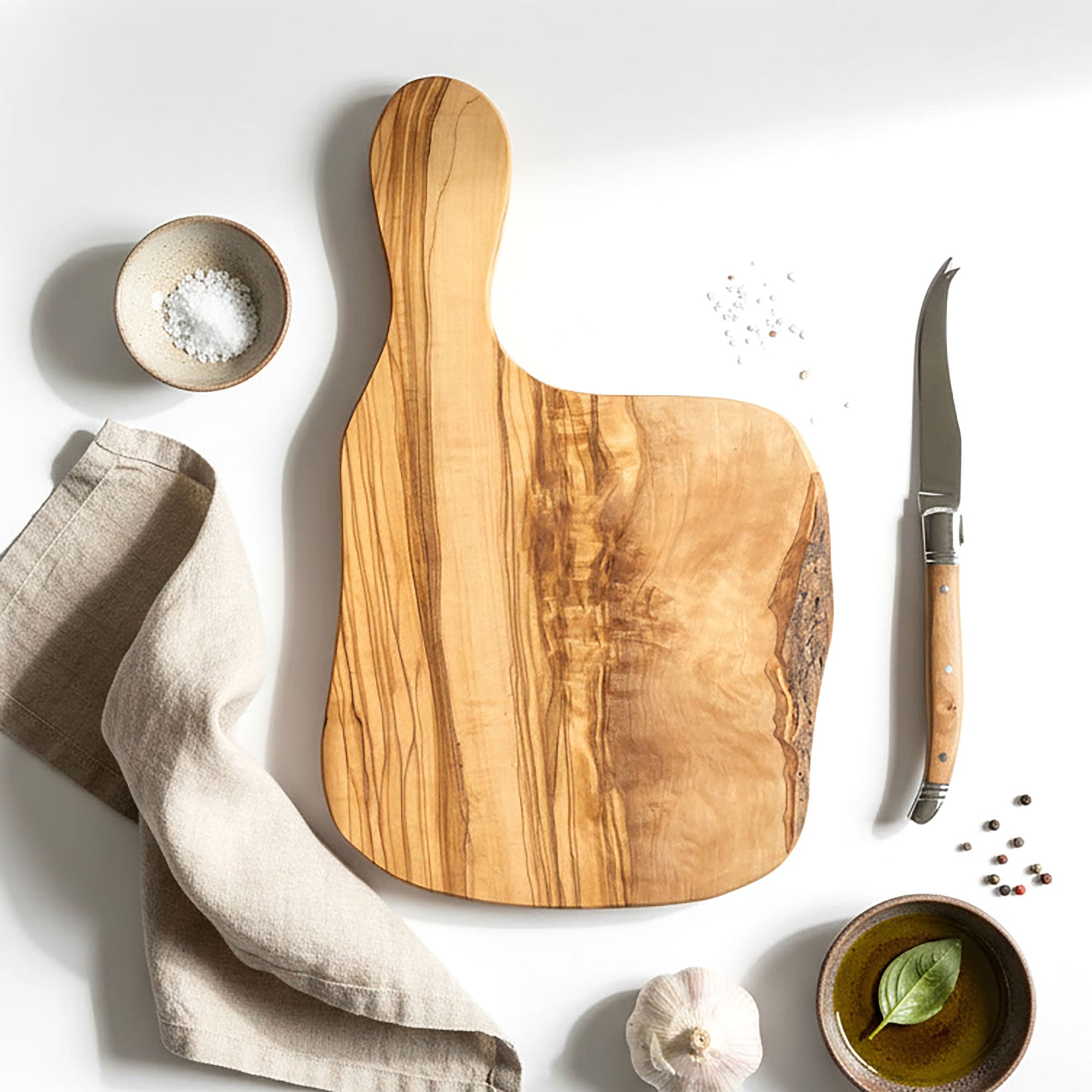 Wooden cutting board with knife, salt, pepper, and garlic on a white background