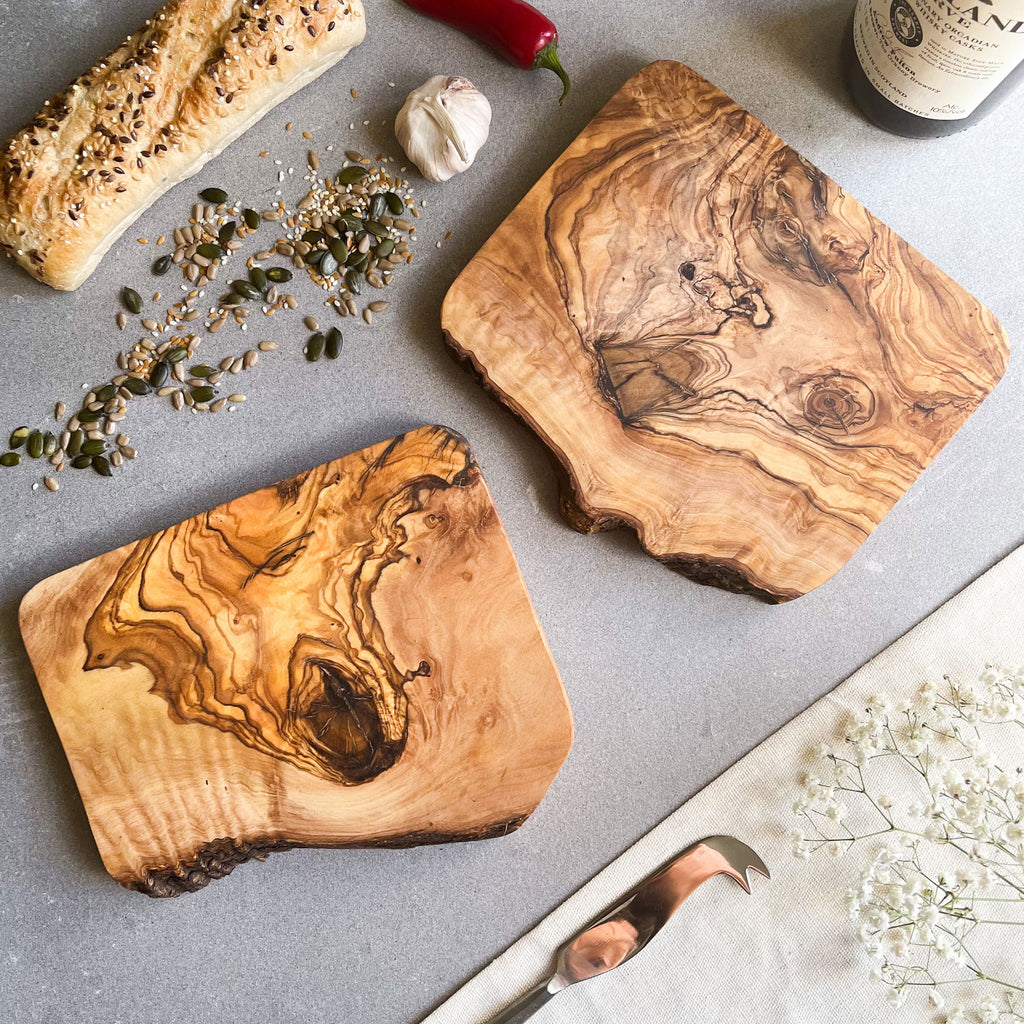 two rustic olive wood boards on a grey surface with cooking accessories and food products