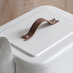 White dog food bin with a brown leather handle on a wooden floor.