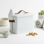 White pet treat container with brown handle on a white surface with pet toys and bones.