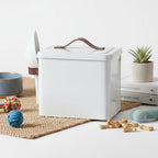 White pet food storage container with a brown handle on a table with dog toys and treats.