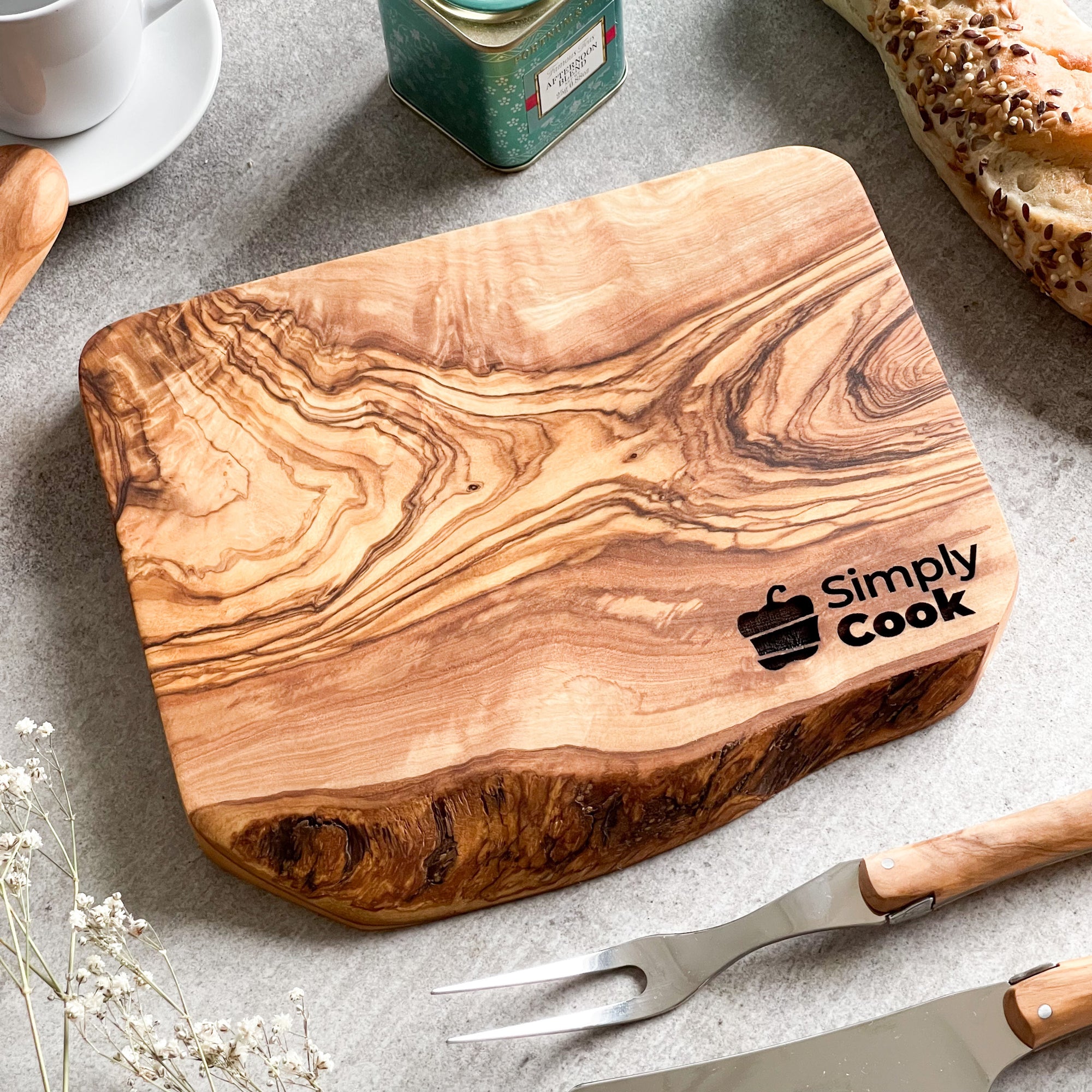 An olive wood chopping/cheese board with a branded logo engraved on it, displayed on a table with some food items.