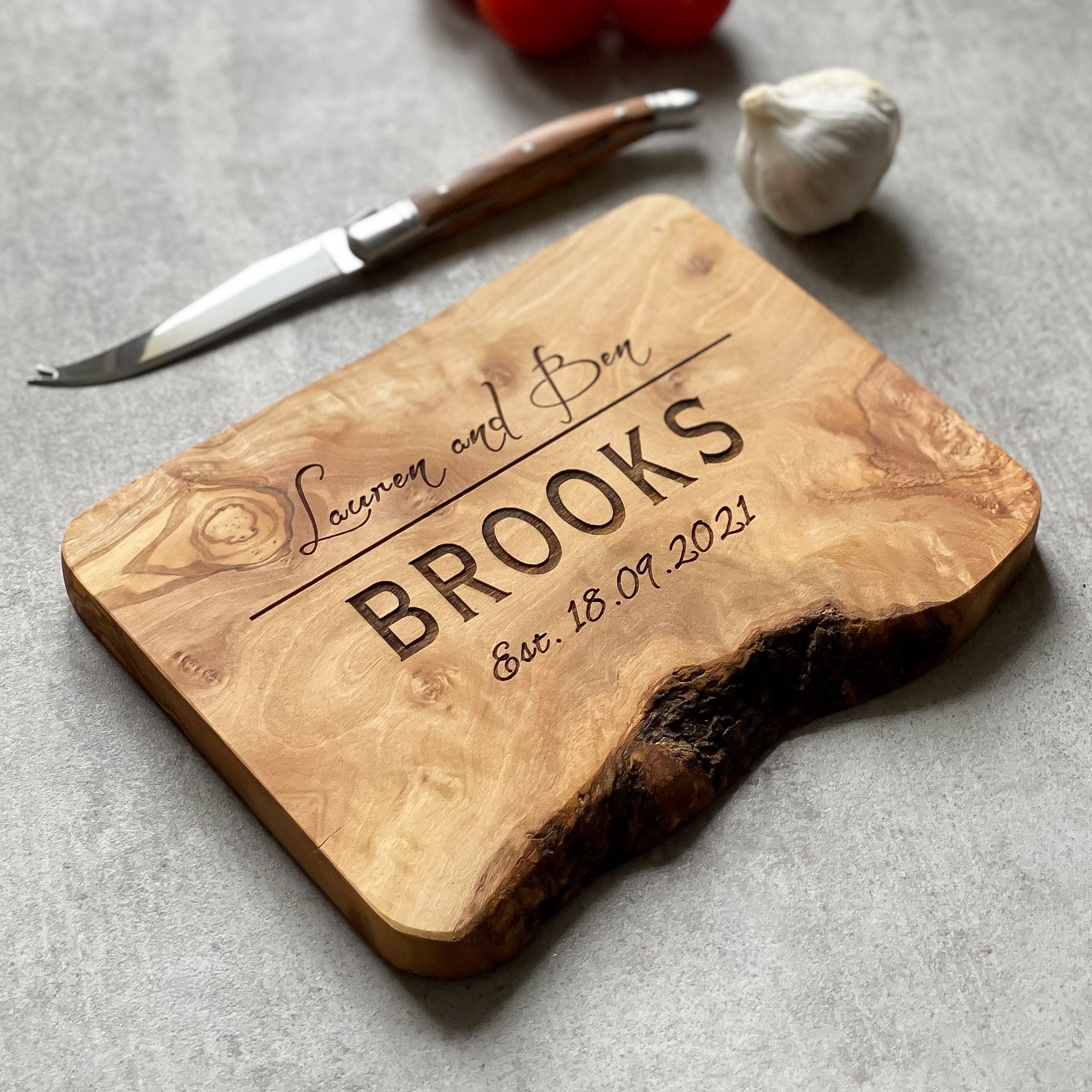 Wooden cutting board with engraved text on a grey surface with knife, garlic and red pepper.