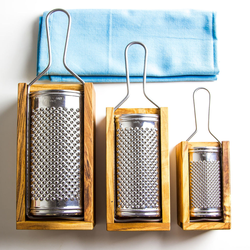 a trio of olive wood hard cheese graters with olive wood boxes and stainless steel grating surface in 3 sizes with a blue napkin