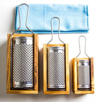 a trio of olive wood hard cheese graters with olive wood boxes and stainless steel grating surface in 3 sizes with a blue napkin