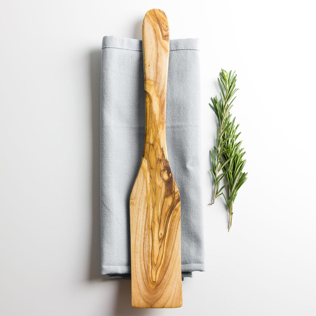 an olive wood spatula on a napkin with some herbs
