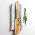 an olive wood spatula on a napkin with some herbs