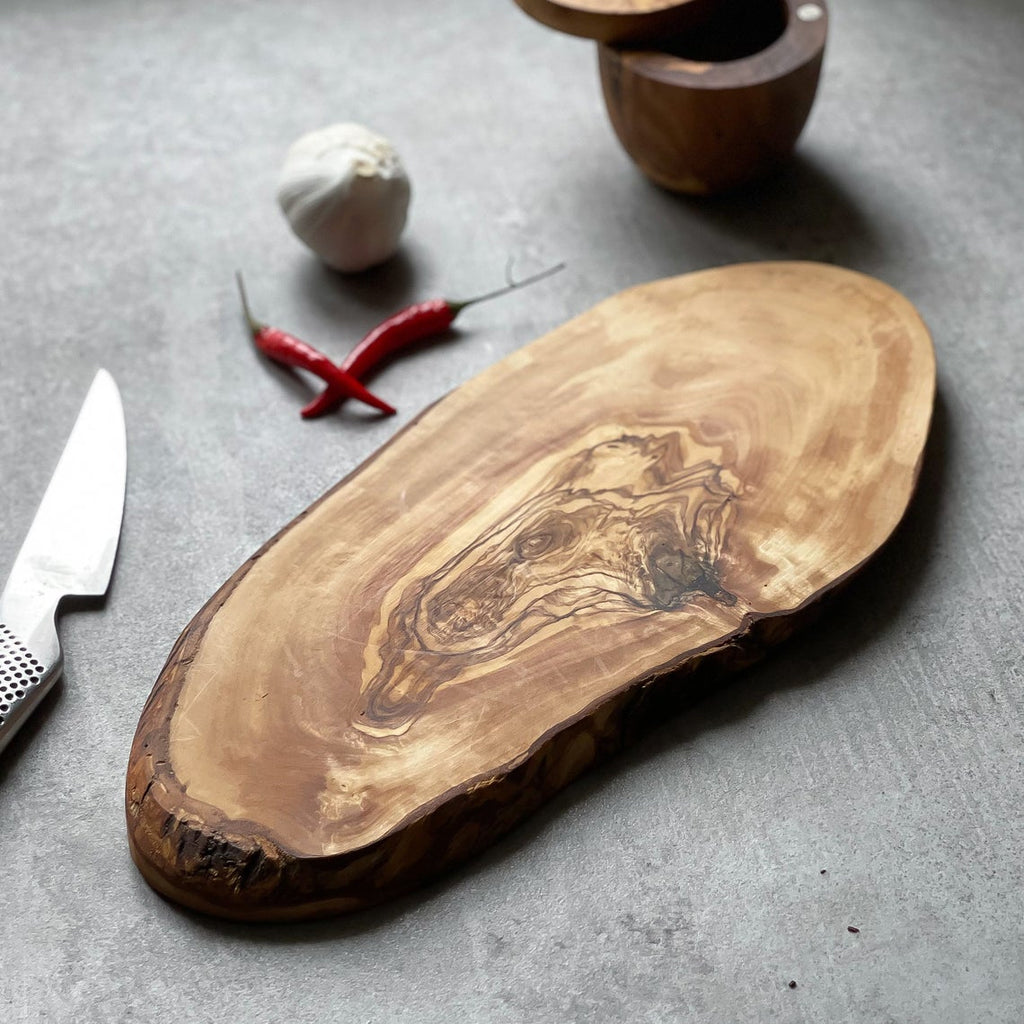 a rustic olive wood board on a grey surface with some chillies, garlic, a knife and salt pot