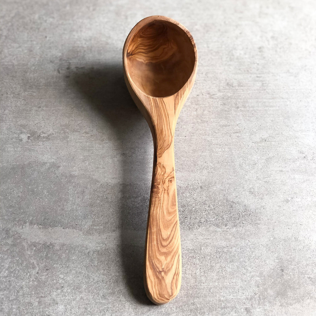 a olive wood ladle resting on a light grey surface