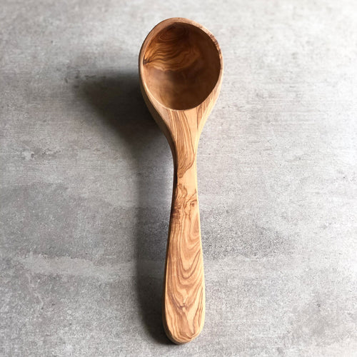 a olive wood ladle resting on a light grey surface