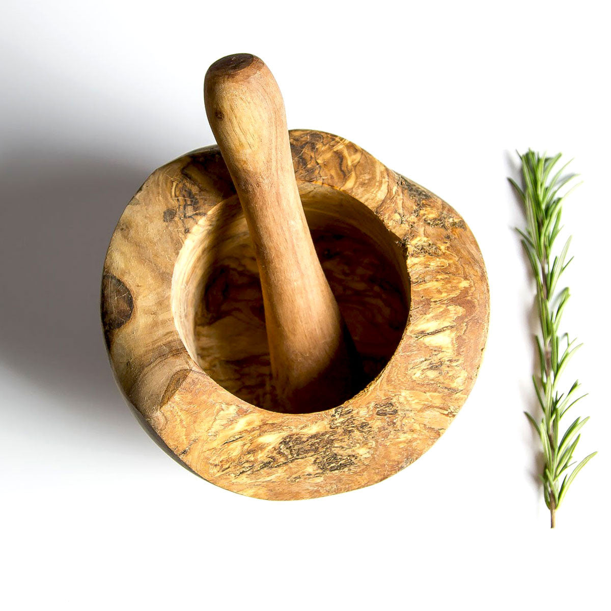 a rustic olive wood pestle and mortar on a white surface with some herbs