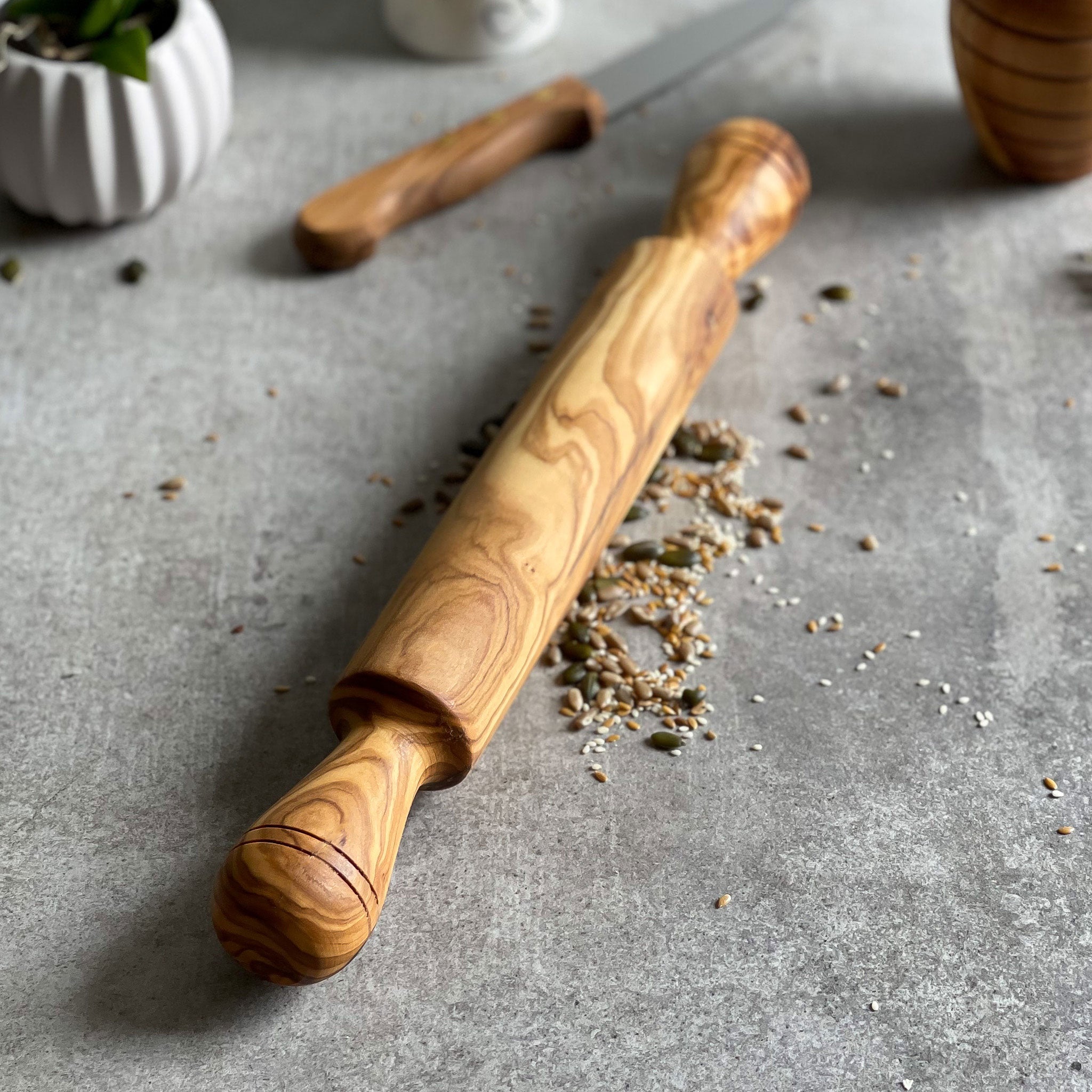 traditional style olive wood rolling pin resting on a grey surface.